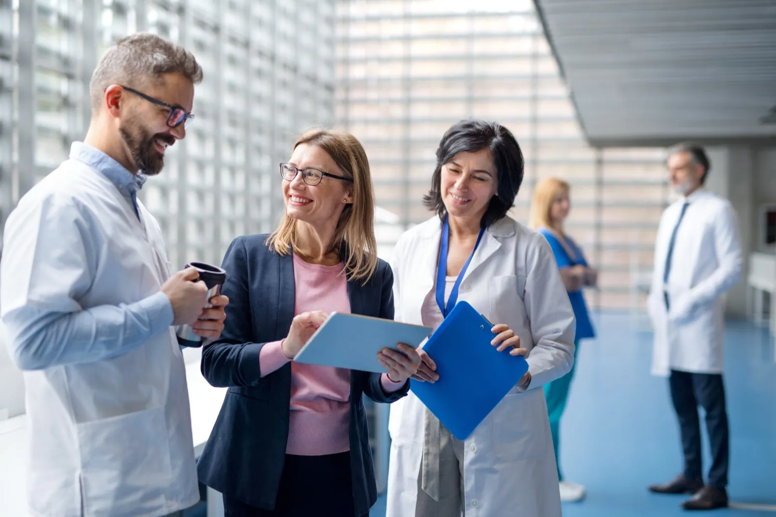 Gruppo di professionisti in camice e abito conversa nell'atrio di una struttura sanitaria.
