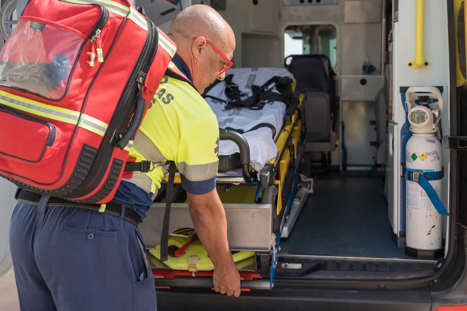 Soccorritore in divisa ad alta visibilità prepara la barella all'interno di un'ambulanza.