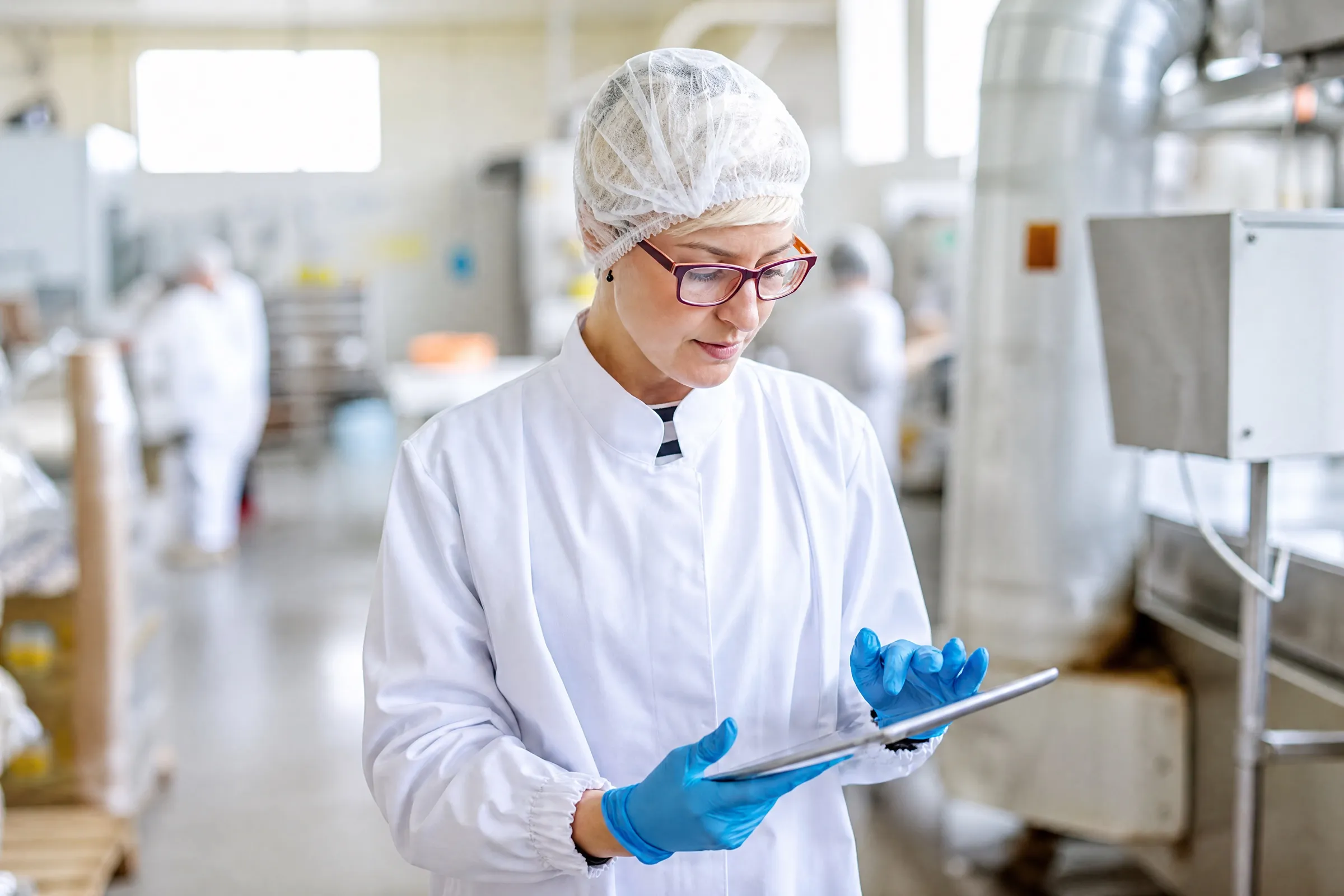 Tecnica di laboratorio in camice e cuffia che consulta un tablet in reparto